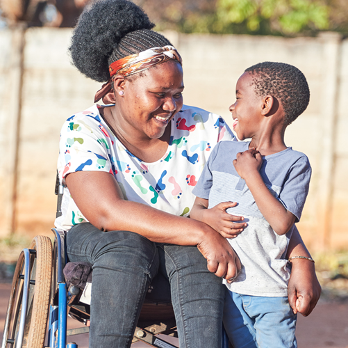 A woman using a wheelchair smiles and talks with a young child outdoors