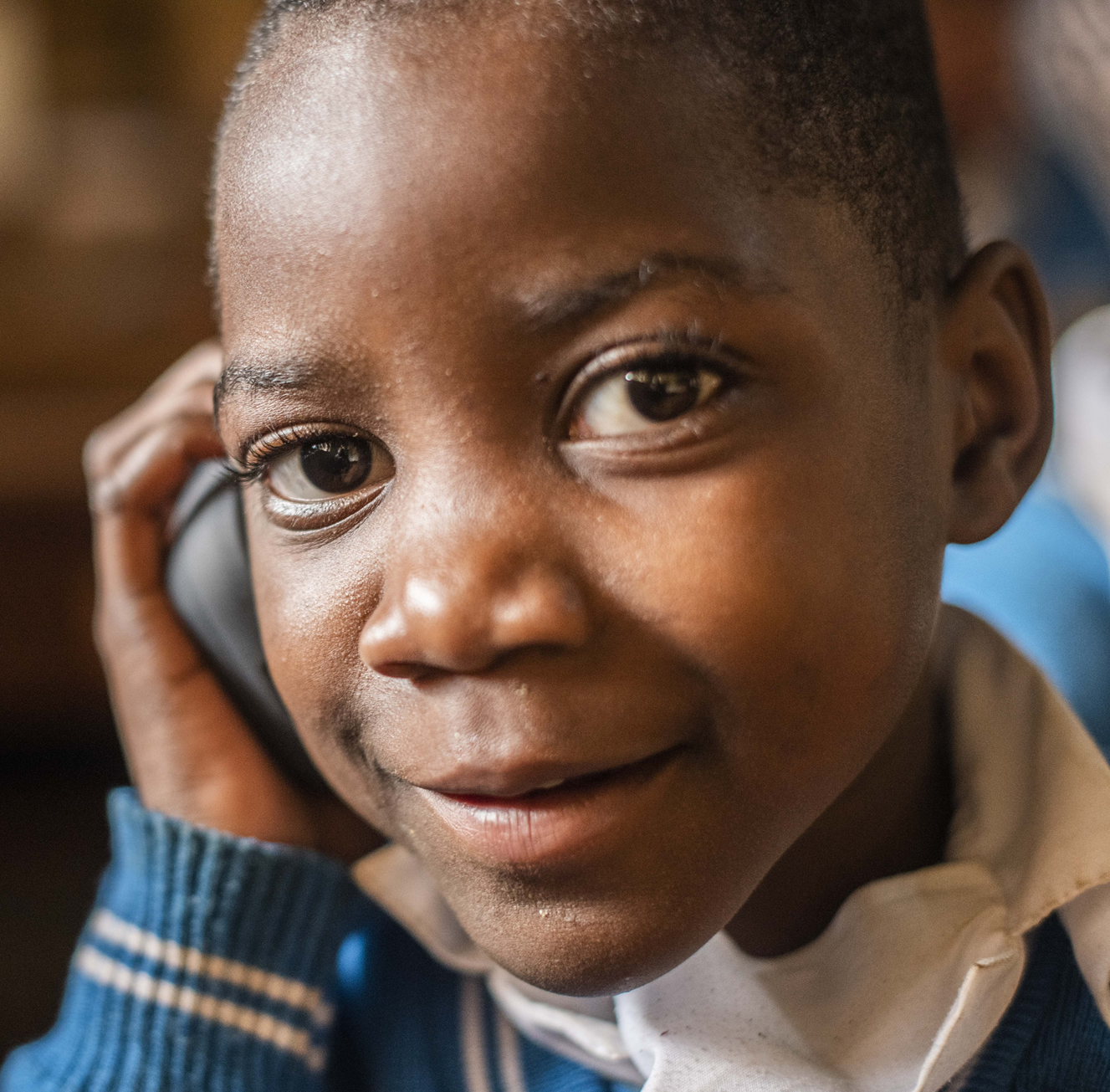 Close-up of a child smiling while holding a mobile phone to their ear