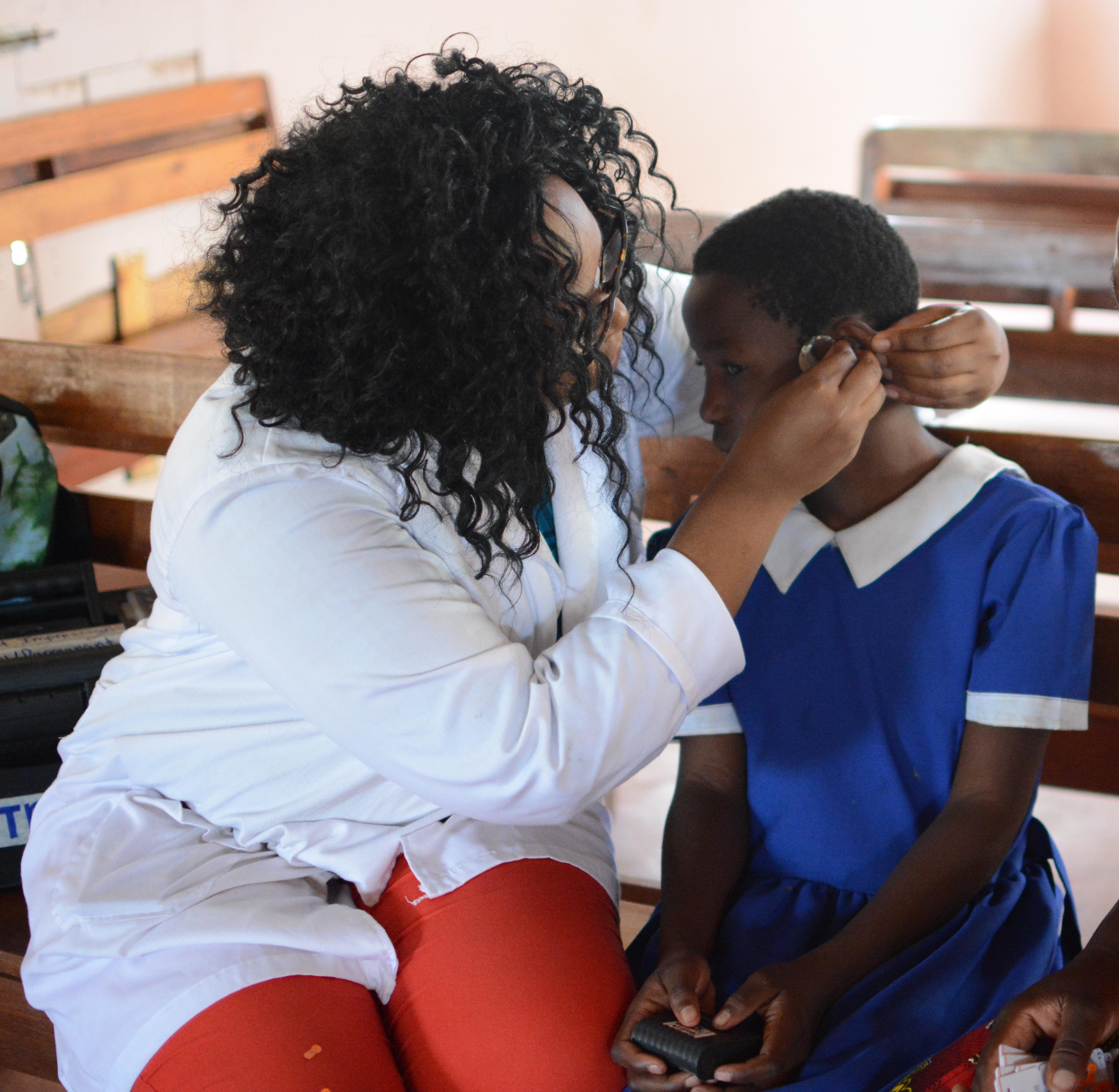An adult helps a child adjust a hearing aid while another person looks on