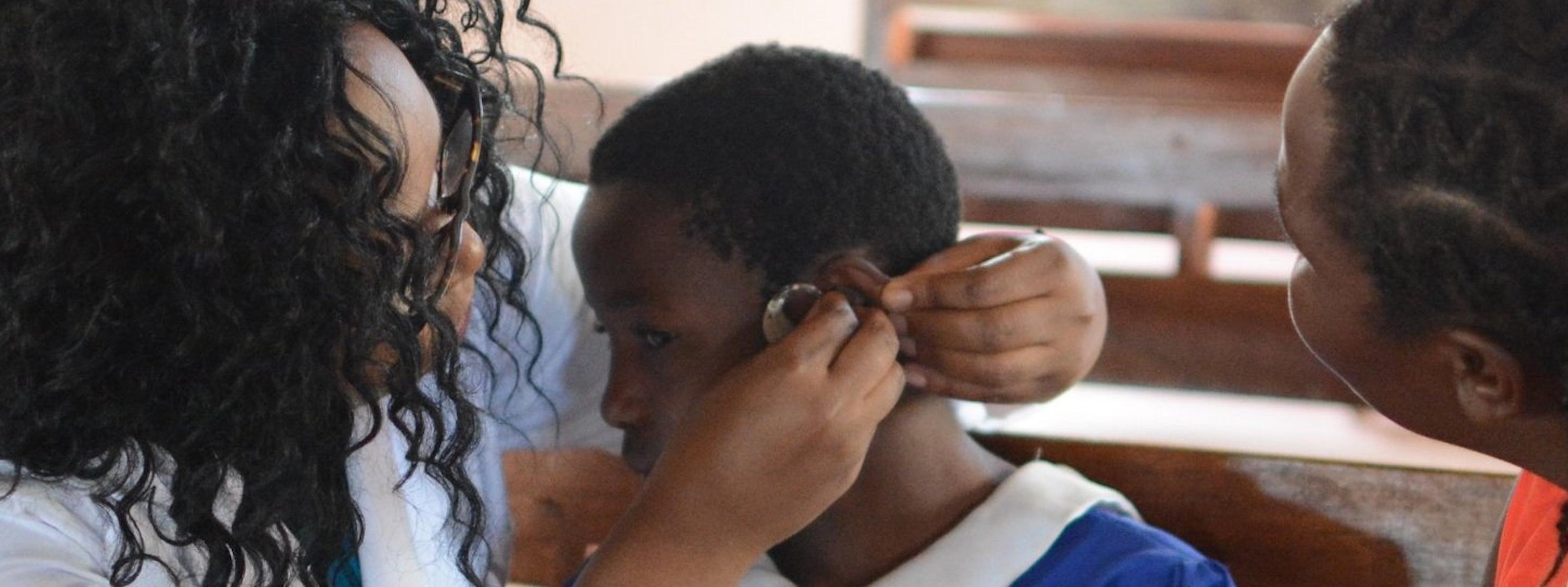 An adult helps a child adjust a hearing aid while another person looks on