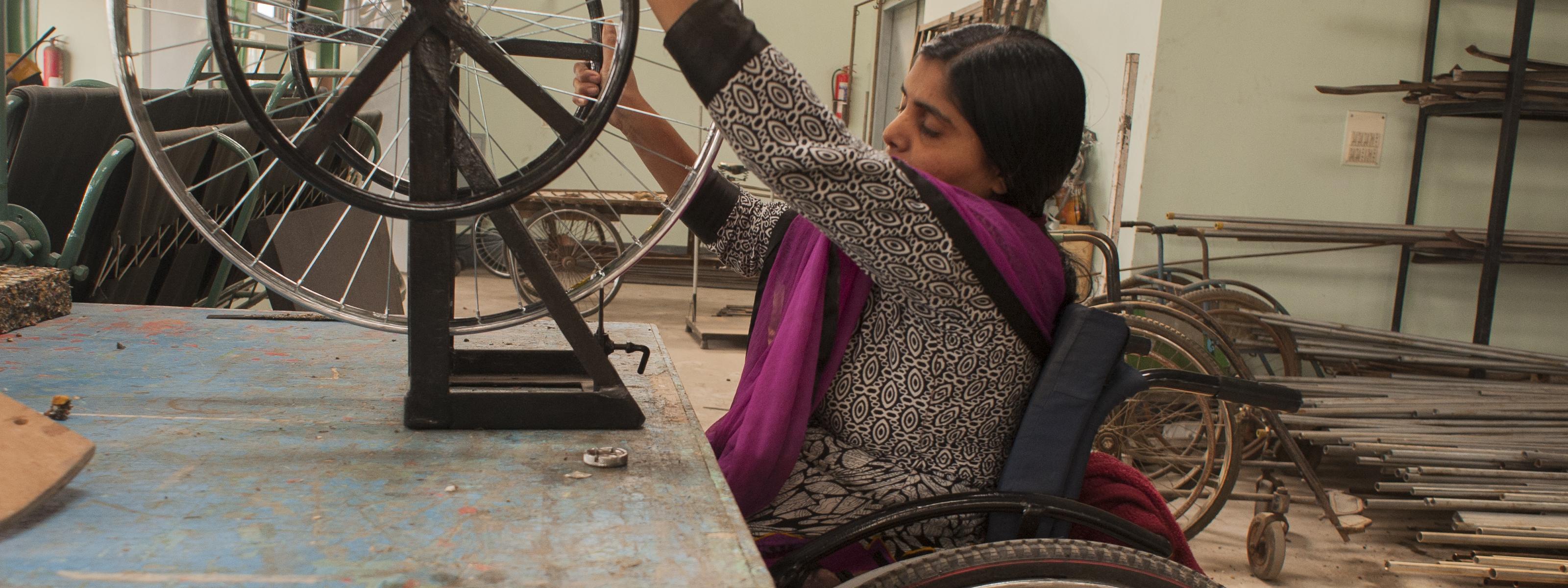 Woman using a wheelchair works in a workshop, adjusting a wheelchair wheel on a repair stand