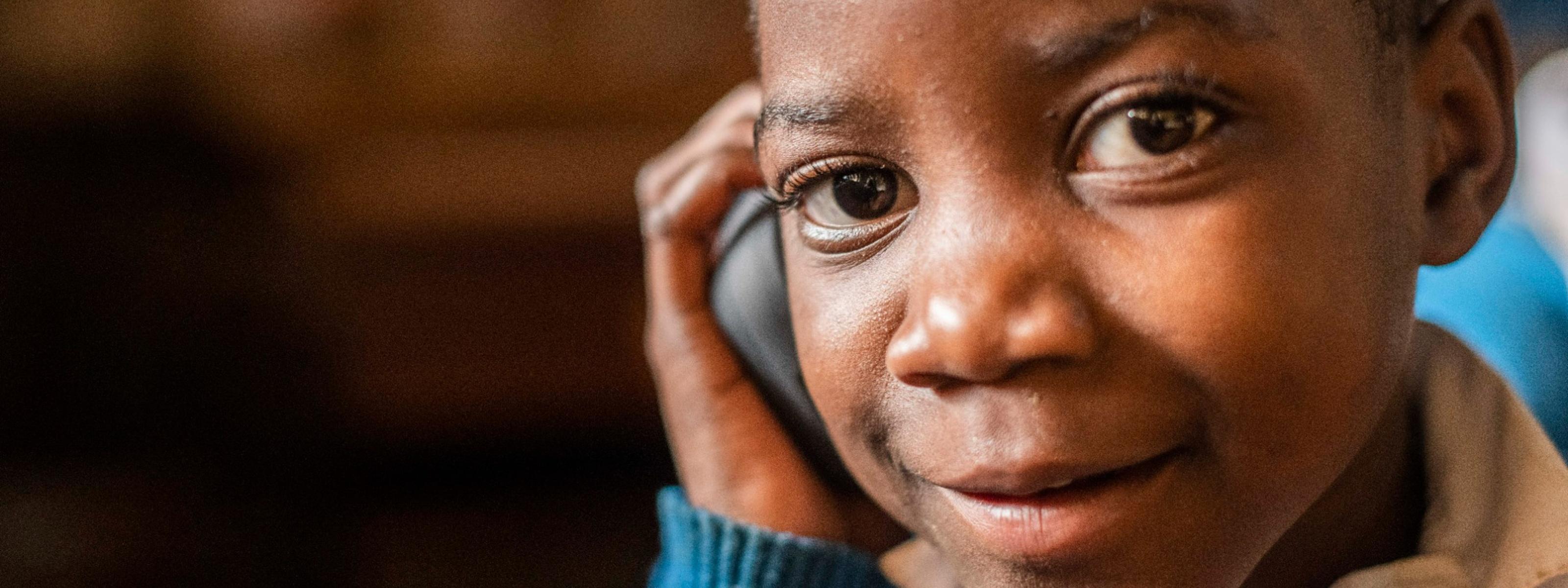 Close-up of a child smiling while holding a mobile phone to their ear