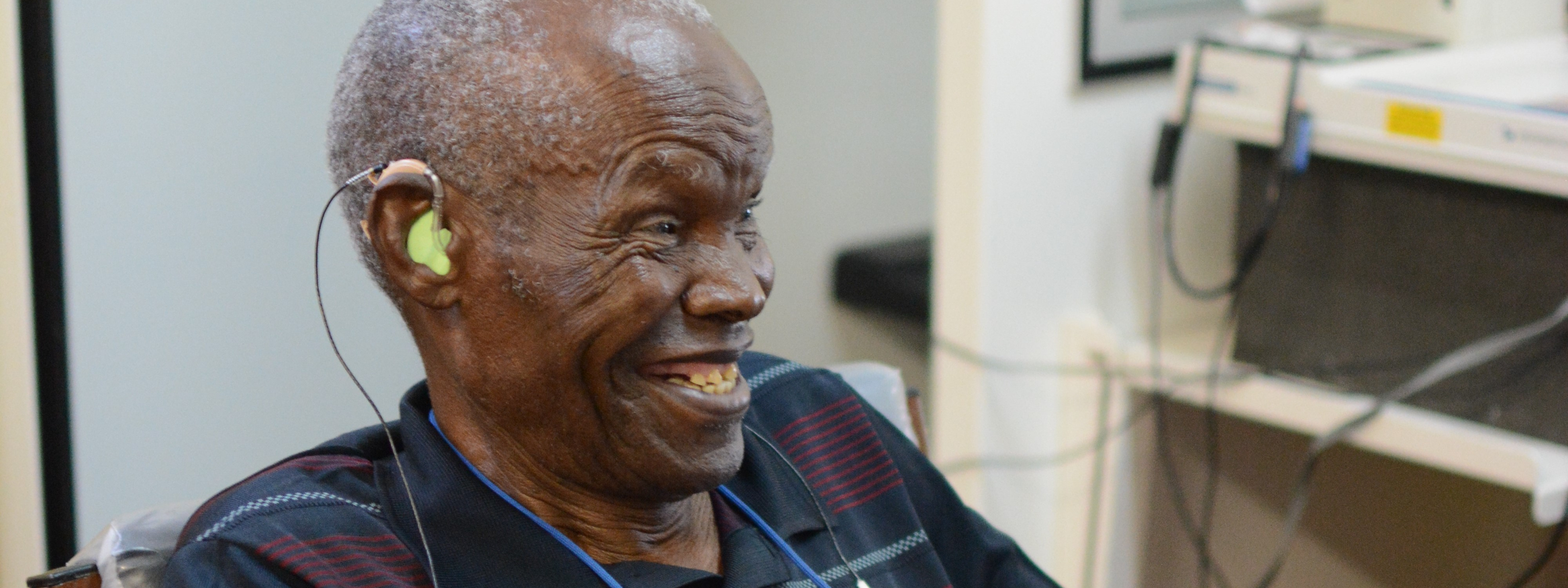 Older man smiling while wearing a hearing aid during a hearing test in a clinic